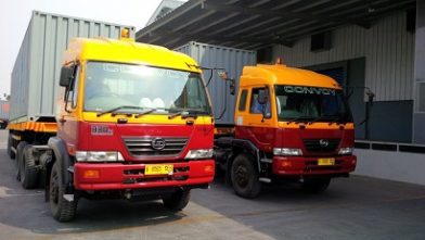 Dua truk kargo sedang parkir di depan sebuah gudang usaha distribusi